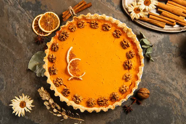 Pumpkin pie with walnuts and orange slices near spices, herbs and candles, thanksgiving centerpiece — Stock Photo