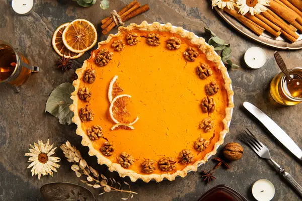 Simboli del Ringraziamento, torta di zucca con noci e fette di arancia vicino a spezie, erbe aromatiche e tè caldo — Foto stock