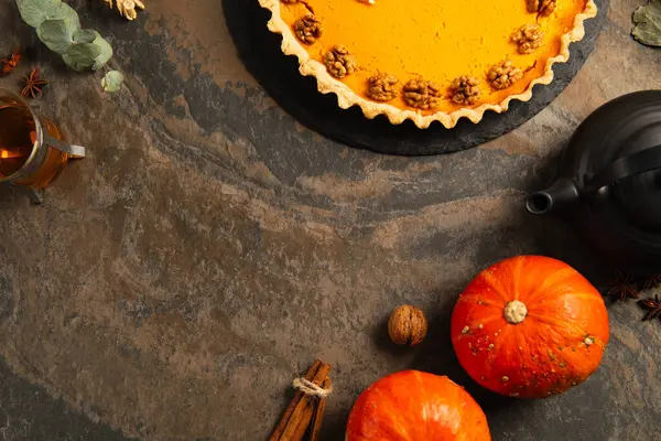 Pastel de calabaza de acción de gracias con nueces cerca de calabazas de naranja maduras, especias y té caliente en la mesa de piedra - foto de stock