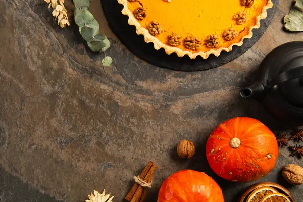 Torta de abóbora com nozes perto de abóboras maduras, especiarias e bule de chá na mesa de pedra, configuração de ação de graças — Fotografia de Stock