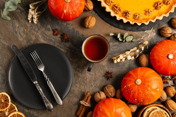 Thanksgiving backdrop with autumnal objects, cutlery on black plate near gourds and pumpkin pie — Stock Photo