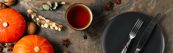 Xícara de chá aromático perto de abóboras de laranja e talheres em placa de cerâmica preta, ação de graças, banner — Fotografia de Stock