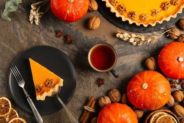Thanksgiving  pumpkin pie on black plate near warm tea and orange pumpkins on decorated stone table — Stock Photo
