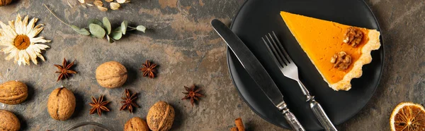 Action de grâces, assiette noire avec tarte à la citrouille et couverts près des noix et épices aux herbes, bannière — Photo de stock
