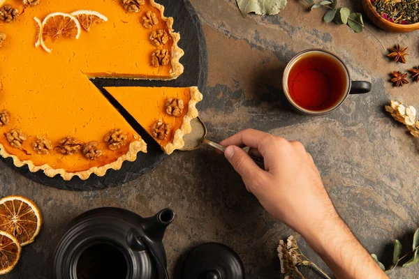 Cropped view of man taking piece of thanksgiving pumpkin pie near black teapot on rough stone table — Stock Photo