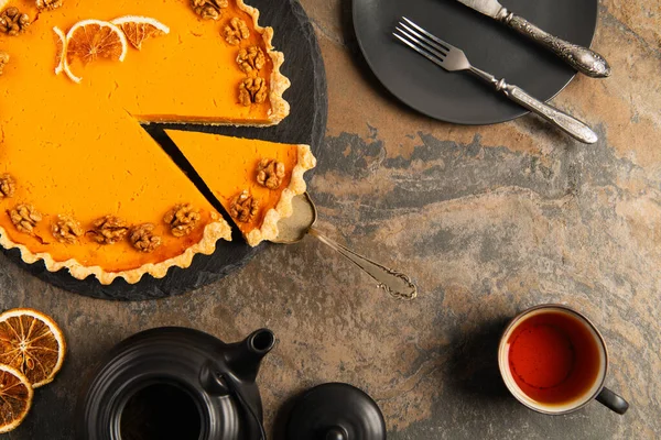 Thanksgiving pumpkin pie near cup of tea and black tableware with vintage cutlery on stone surface — Stock Photo