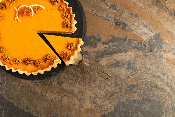 Cake spatula near thanksgiving pie garnished with orange slices and walnuts on textured stone table — Stock Photo