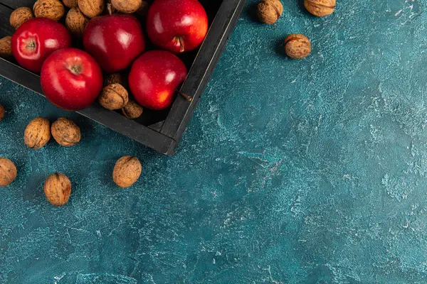 Black wooden tray with red apples and walnuts on blue textured surface, thanksgiving setting — Stock Photo