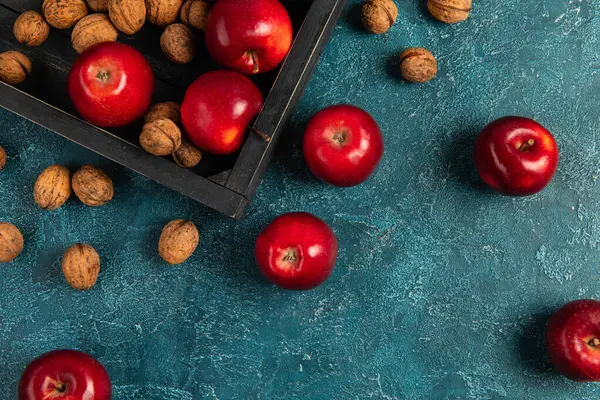 Conceito de ação de graças, bandeja de madeira preta com maçãs vermelhas e nozes na superfície texturizada azul — Fotografia de Stock