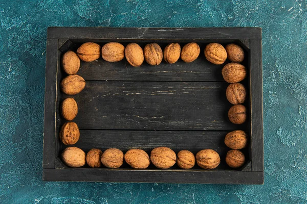 Autumnal backdrop with walnuts in black wooden tray on blue textured surface, thanksgiving concept — Stock Photo