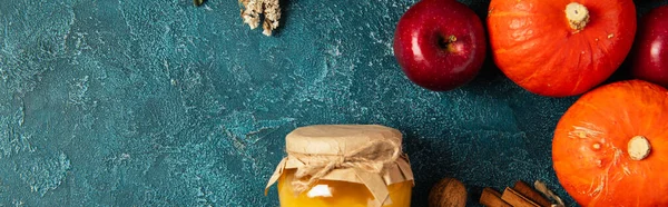 Pumpkins and red apple near jar of honey on blue textured surface, thanksgiving still life, banner — Stock Photo