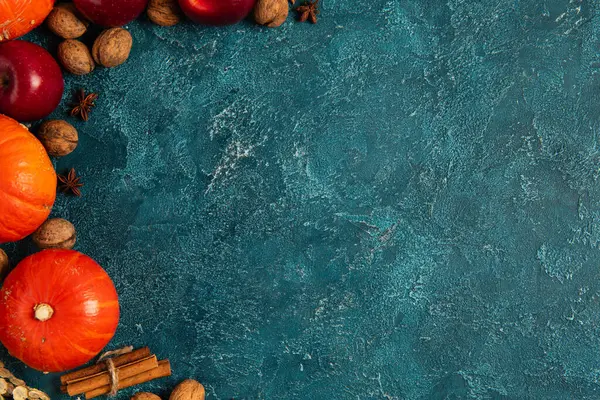 Помаранчеві гарбузи біля червоних яблук і волоських горіхів на синьому текстурованому фоні, концепція подяки — стокове фото