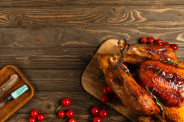 Erntedank-Essen, gebratener Truthahn neben roten Kirschtomaten und Kochutensilien auf Holztisch — Stockfoto