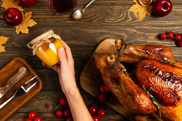 Cropped view of man with jar of honey near thanksgiving turkey on wooden table with autumnal decor — Stock Photo