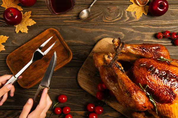 Vista ritagliata dell'uomo con forchetta culinaria e coltello vicino al tacchino del Ringraziamento sul tavolo di legno decorato — Foto stock
