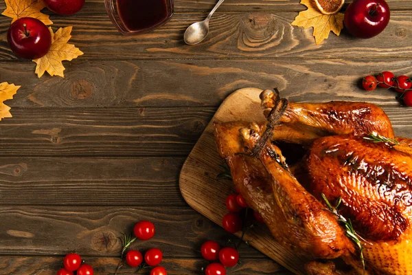 Thanksgiving still life, roasted turkey near cherry tomatoes and maple leaves on rustic wooden table — Stock Photo