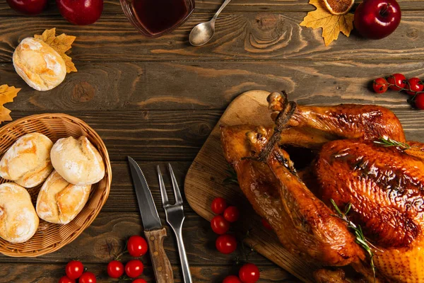 Thanksgiving turkey and freshly baked buns near cherry tomatoes and cutlery on rustic wooden table — Stock Photo