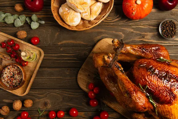 Thanksgiving turkey and freshly baked buns near red cherry tomatoes and spices on wooden tabletop — Stock Photo