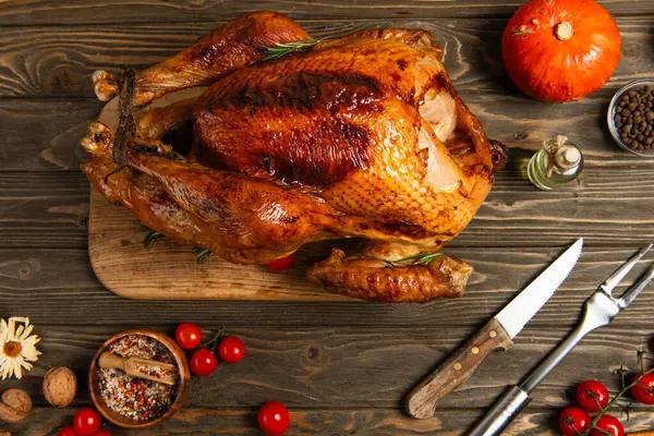 Delicious thanksgiving, roasted turkey near cherry tomatoes, spices and cutlery on wooden tabletop — Stock Photo