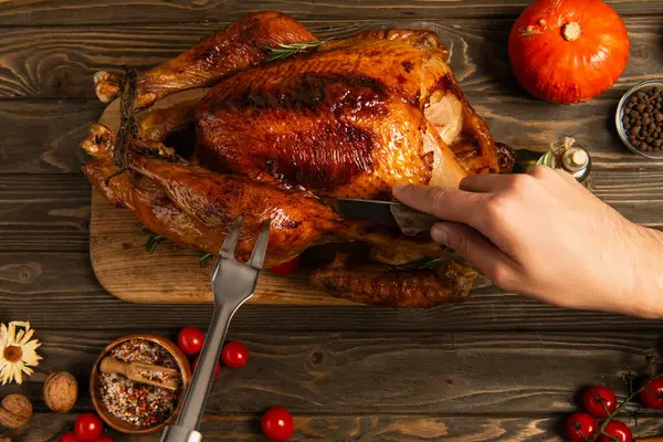 Cropped view of man with knife and culinary fork cutting thanksgiving turkey on decorated table — Stock Photo