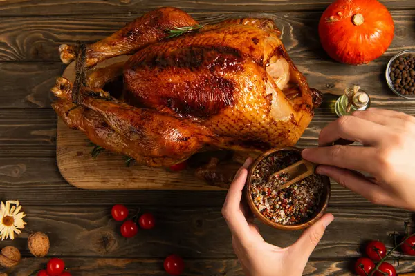 Cropped view of holding spices in wooden bowl near thanksgiving turkey on decorated festive table — Stock Photo