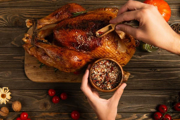Cropped view of man seasoning roasted turkey on wooden table, thanksgiving dinner preparation — Stock Photo