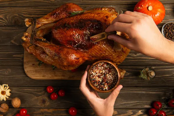 Thanksgiving dinner, partial view of man seasoning turkey near cherry tomatoes on wooden table — Stock Photo