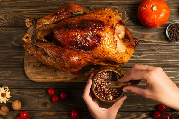 Thanksgiving concept, cropped view of man holding wooden bowl with spices near roasted turkey — Stock Photo