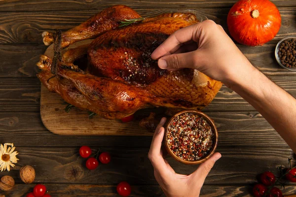Cropped view of man with wooden bowl seasoning grilled turkey for festive thanksgiving dinner — Stock Photo