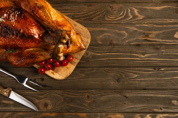 Thanksgiving theme, grilled turkey on cutting board near cherry tomatoes and cutlery on wooden table — Stock Photo