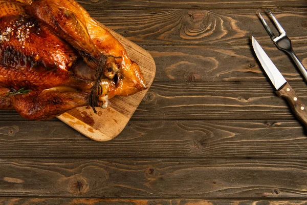 Delicious grilled turkey on cutting board near cutlery on wooden tabletop, thanksgiving background — Stock Photo
