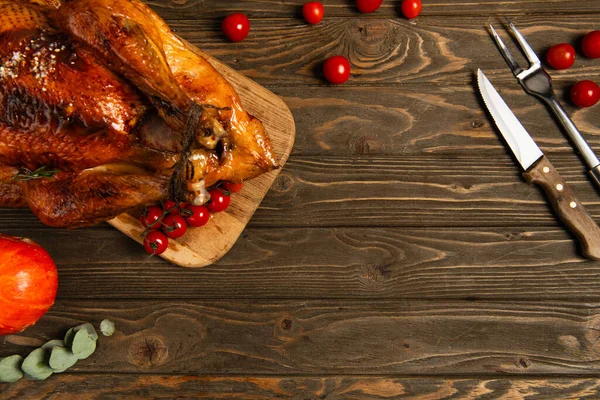 Delicious thanksgiving, roasted turkey and cherry tomatoes near cutlery on textured wooden table — Stock Photo