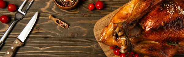 Roasted thanksgiving turkey near spices, cutlery and red cherry tomatoes on wooden tabletop, banner — Stock Photo