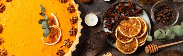 Thanksgiving setting, pumpkin pie with walnuts and orange slices near spices on stone table, banner — Stock Photo