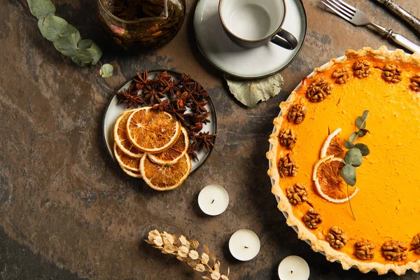 Steintisch mit Erntedank-Kürbiskuchen neben Tee und Gewürzen mit Orangenscheiben, herbstliches Thema — Stockfoto