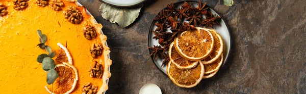 Erntedank-Kürbiskuchen neben getrockneten Orangenscheiben und aromatischen Gewürzen auf Steintischplatte, Banner — Stockfoto