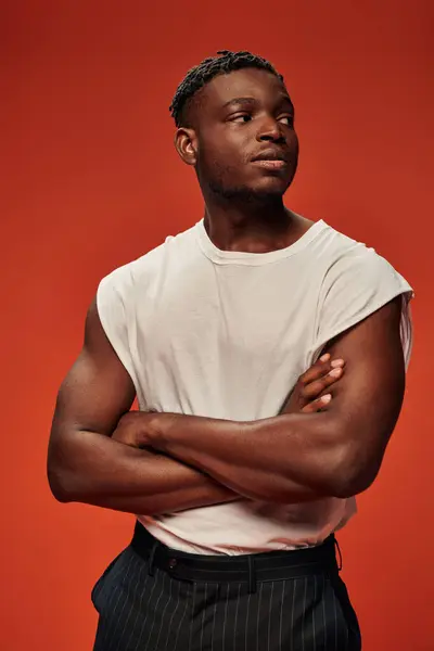 Young self-confident african american man in white tank top looking away with folded arms on red — Stock Photo