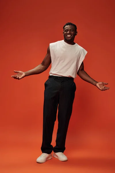 Happy african american man in trendy casual clothes showing welcoming gesture with open arms on red — Stock Photo