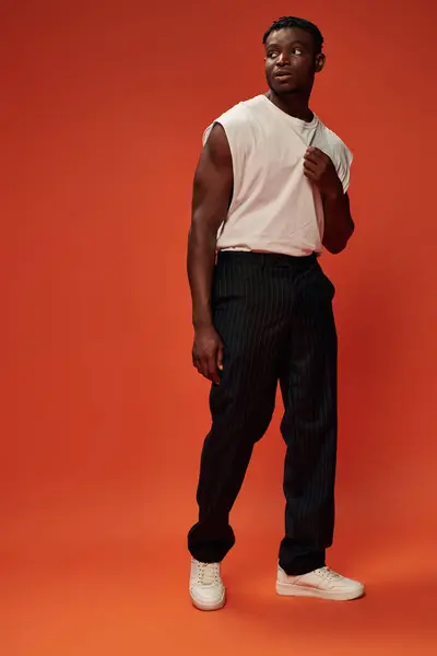 Atlético afroamericano hombre en pantalones negros y camiseta blanca mirando hacia otro lado en rojo, longitud completa - foto de stock