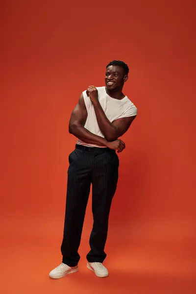 Повна довжина радісного афроамериканця в чорних штанях, що стоять на червоному і помаранчевому тлі — стокове фото