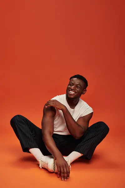 Excited stylish african american man sitting and laughing with closed eyes, red and orange backdrop — Stock Photo