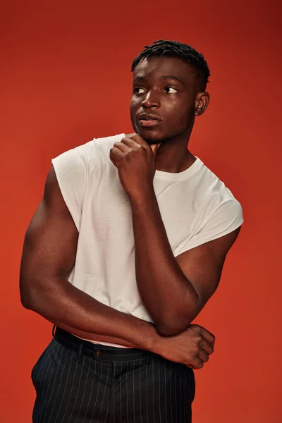 Thoughtful african american male model in white tank top looking away while standing on red — Stock Photo