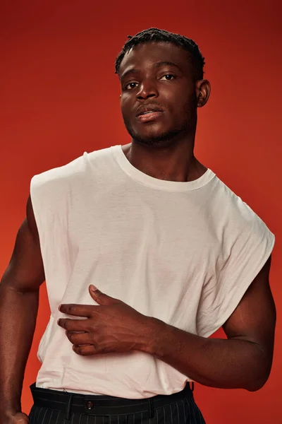 Carismático hombre afroamericano elegante en camiseta blanca mirando a la cámara en rojo, estilo moderno - foto de stock
