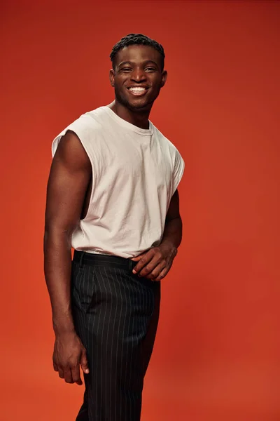Задоволений афроамериканський чоловік у модному вуличному одязі, посміхаючись на камеру на червоному, позитивно — стокове фото