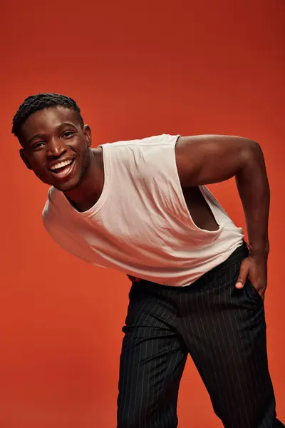 Joyful african american man with hand in pocket leaning forward and smiling at camera on red — Stock Photo