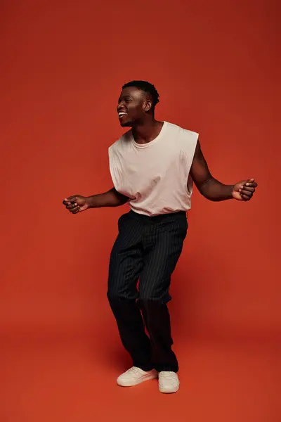 Дивовижний і щасливий афроамериканський чоловік у стильному вбранні, дивлячись далеко на червоний і помаранчевий фон — стокове фото