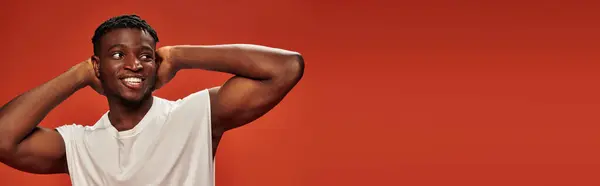 Smiley et chaud afro-américain gars debout avec les mains derrière la tête et regardant loin sur rouge, bannière — Photo de stock