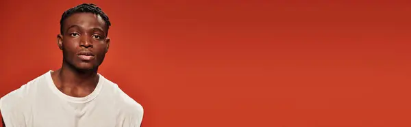 Modelo masculino afroamericano elegante de buen aspecto en camiseta blanca mirando la cámara en rojo, bandera — Stock Photo