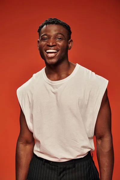 Young excited african american male model in white tank top laughing and looking at camera on red — Stock Photo