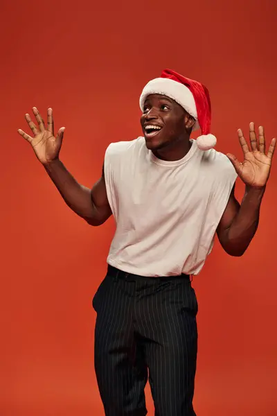 Amazed and overjoyed african american man in santa hat showing wow gesture and looking away on red — Stock Photo